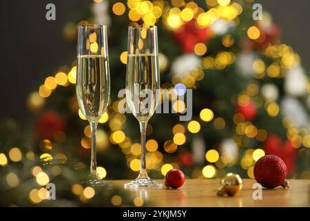 Champagne en verres et ornements festifs sur table en bois contre les lumières de Noël floues, espace pour le texte. Effet bokeh Banque D'Images