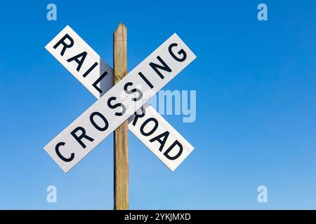 Panneau blanc d'avertissement de passage à niveau isolé sur le ciel bleu. Concept de sécurité ferroviaire, de transport et de circulation. Banque D'Images