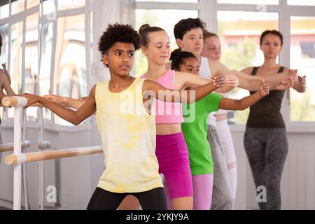 Adolescent afro-américain maîtrisant demi-plie à la barre au cours de ballet Banque D'Images