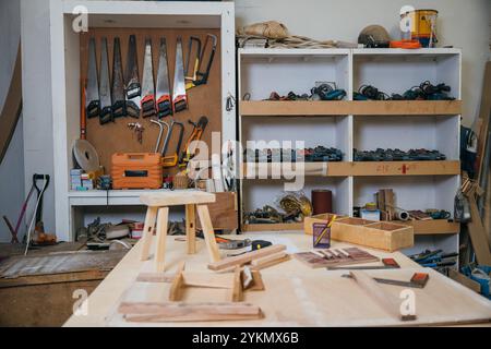 Etabli en bois vintage dans un atelier encombré avec divers outils et équipements. Les vieux outils s'accrochent Banque D'Images