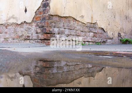 Mur de briques avec une fissure dedans et une flaque d'eau reflétant le mur. Le reflet du mur est déformé et flou, donnant l'impression de Banque D'Images