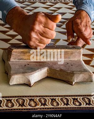 Gros plan des mains d'un artisan qualifié sculptant des motifs ornés sur un bloc de bois Banque D'Images