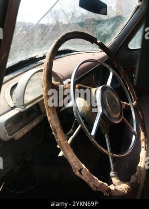 Une vue détaillée de l'intérieur détérioré d'une voiture ancienne abandonnée, mettant en évidence un volant cassé. Capture l'essence de la pourriture et le passa Banque D'Images