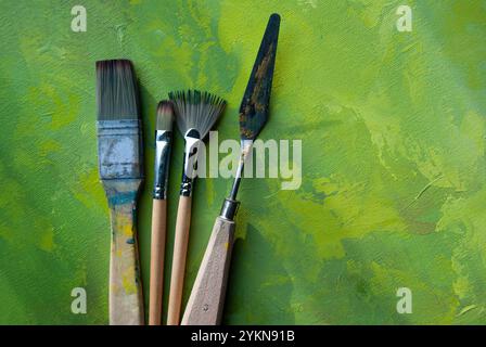 Pinceaux créatifs placés sur une toile colorée avec des traits acryliques verts, blancs et or, mettant en valeur un design abstrait. Banque D'Images