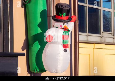 Un bonhomme de neige gonflable festif, orné d'un chapeau haut de gamme élégant et d'une écharpe confortable, parfait pour les vacances d'hiver et les célébrations de Noël Banque D'Images