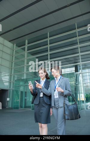 Deux employés de bureau regardant leur téléphone dans un immeuble de bureaux Banque D'Images
