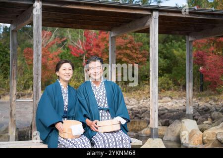Un couple d'âge moyen tenant une baignoire de yukata et une serviette à un onsen ryokan en automne Banque D'Images