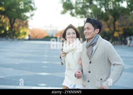 Couple dans la vingtaine courir dans un parc à la fin de l'automne Banque D'Images