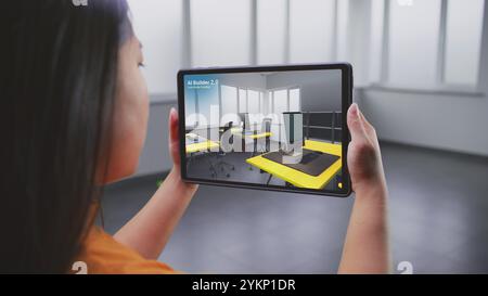 Designer féminin asiatique utilise l'ordinateur tablette et l'application de design d'intérieur de réalité virtuelle pour concevoir l'espace de travail de bureau. L'écran de la tablette montre le logiciel ai Builder scannant et créant un design avec des meubles 3D. Banque D'Images