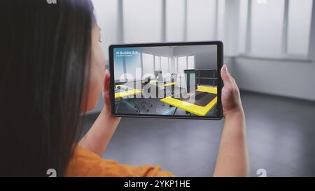 Designer féminin asiatique utilise l'ordinateur tablette et l'application de design d'intérieur de réalité virtuelle pour concevoir l'espace de travail de bureau. L'écran de la tablette montre le logiciel ai Builder scannant et créant un design avec des meubles 3D. Banque D'Images