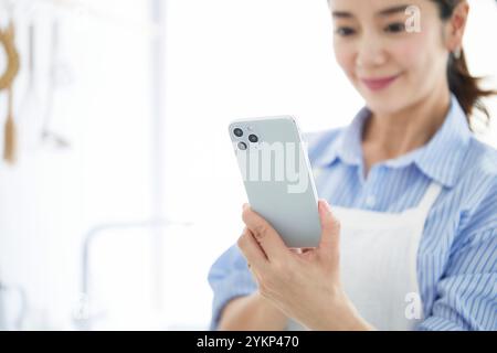 Femme regardant son téléphone en cuisinant dans la cuisine Banque D'Images