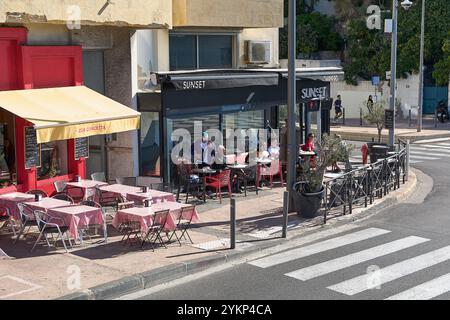 Viladecans. Espagne - 19 novembre 2024 : CAF en plein air dans un coin ensoleillé à Marseille, avec des tables et des chaises rouges et blanches, et des clients dégustant des boissons Banque D'Images