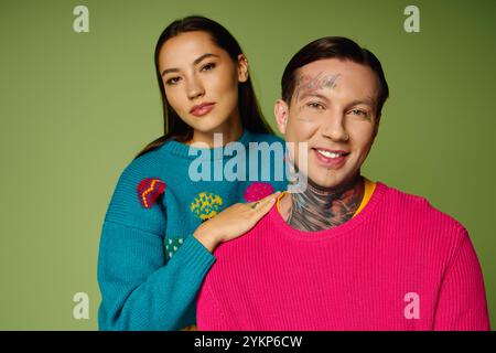 Un couple élégant sourit, mettant en valeur leurs tenues colorées et leurs tatouages dans une scène joyeuse. Banque D'Images