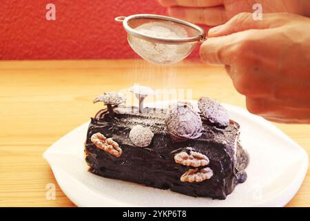 Saupoudrer à la main de sucre en poudre dans le gâteau de Noël de la Yule au chocolat fraîchement cuit Banque D'Images