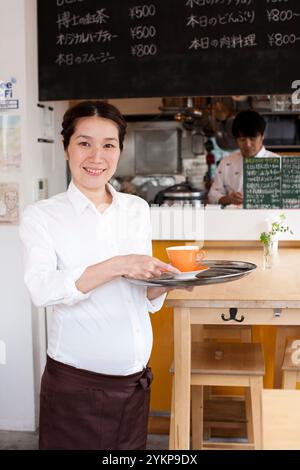 Femme enceinte souriante et servant dans un restaurant avec une tasse de café dans la main Banque D'Images