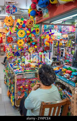 Une femme âgée de Singapour assise à son étal de marché avec un ventilateur soufflant sur ses jouets de spin à Singapour Banque D'Images