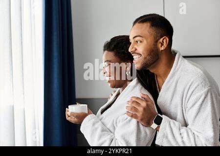 Un couple joyeux partage un moment tendre, sirotant des boissons chaudes et embrassant dans leur chambre d'hôtel. Banque D'Images