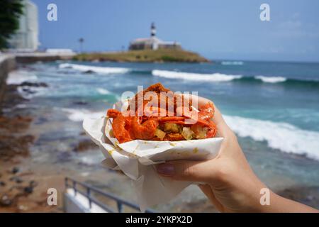 Plat traditionnel Acaraje et cuisine de rue du nord-est du Brésil avec le phare de Farol da Barra et la baie de tous les Saints en arrière-plan, Salvador de Bah Banque D'Images