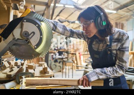 Une femme concentrée travaille avec une scie circulaire dans un jardin à bois vibrant, mettant en valeur son savoir-faire et son attention aux détails. L'ambiance met en évidence ded Banque D'Images