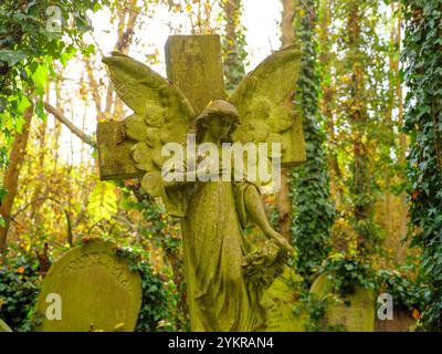 Ange en pierre sur la croix d'une pierre tombale d'une tombe dans le cimetière d'Abney Park, Hackney, Londres, Royaume-Uni Banque D'Images