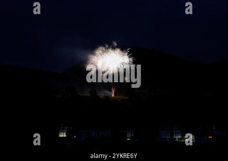 Une fusée de feu d'artifice dans le ciel sur une montagne la nuit, quelques maisons illuminées au premier plan Banque D'Images