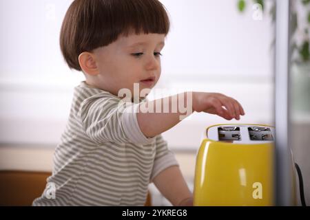 Petit garçon jouant avec le grille-pain dans la cuisine. Situation dangereuse Banque D'Images