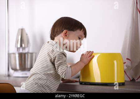 Petit garçon jouant avec le grille-pain dans la cuisine. Situation dangereuse Banque D'Images