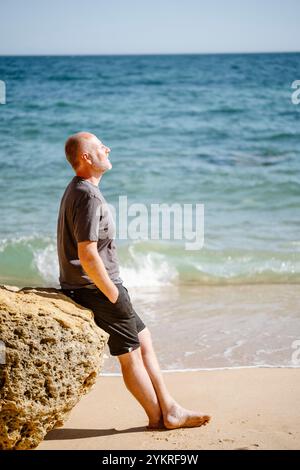 Homme caucasien assis sur un rocher à la plage de São Rafael à Albufeira, Algarve - Portugal Banque D'Images