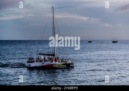 Ambiance nocturne sur l'océan sur la côte sud de Curaçao. Un catamaran avec des touristes revient de son excursion d'une journée à Willemstad et en arrière-plan, vous pouvez voir les bateaux des vendeurs de fruits et légumes vénézuéliens qui retournent au Venezuela depuis le marché flottant de Willemstad. Kaya Wilson Godett, Curaçao, Curaçao, Kòrsou Banque D'Images