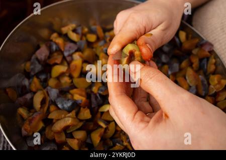 Mains de femme,, coupe avec un couteau aiguisé prunes mûres pour confiture, soft focus Banque D'Images