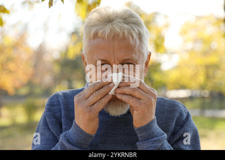 Homme senior avec des tissus soufflant le nez qui coule dans le parc Banque D'Images