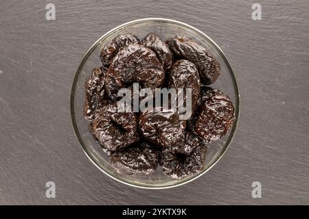 Pruneaux sucrés dans une assiette en céramique sur une pierre d'ardoise, macro, vue de dessus. Banque D'Images