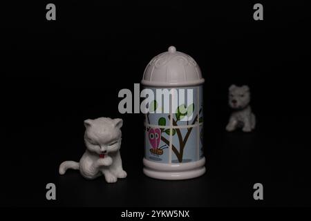 Chat blanc avec petit chien assis près de la colonne morris, jouet de colonne publicitaire en plastique Banque D'Images