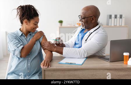 Femme noire souriante se faire vacciner au cabinet du médecin Banque D'Images