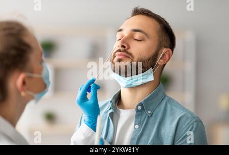 Test PCR du coronavirus nasal. Médecin utilisant un écouvillon pour prélever un échantillon de virus covid chez un jeune type potentiellement infecté Banque D'Images