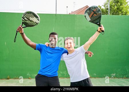 Deux hommes tiennent des raquettes de paddle-tennis et sourient. Ils posent pour une photo sur un court de tennis Banque D'Images