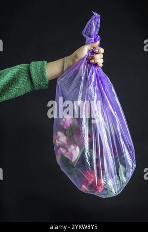 Gros plan pour femmes tenant main sac en plastique avec des fleurs. Isolé sur noir. Concept de gaspillage d'argent Banque D'Images