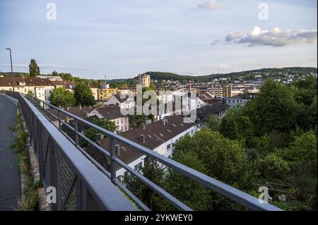 Vue d'une route sécurisée longeant une pente, surplombant une vallée avec des maisons et des arbres dans un ciel partiellement nuageux, chaudière à gaz à Wuppertal Heckinghausen Banque D'Images