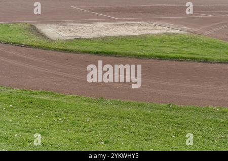 Sablier de saut long et piste de course avec de l'herbe verte sur une journée nuageuse Banque D'Images