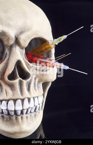 Crâne humain avec des seringues colorées dans le trou des yeux. Isolé sur fond noir Banque D'Images