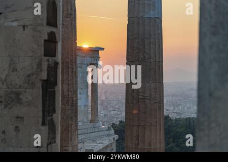 Une photo du coucher de soleil vu à travers les ruines de Propylaea, la porte de l'Acropole d'Athènes, et touchant le sommet du Temple d'Athéna N. Banque D'Images