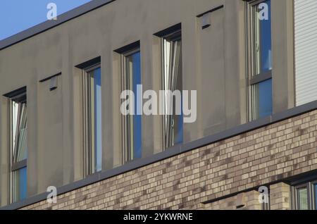 Fenêtres ouvertes sur un bâtiment moderne reflétant le ciel bleu, avec une façade en briques Banque D'Images