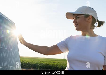 Femme touche un panneau solaire au coucher du soleil. Banque D'Images