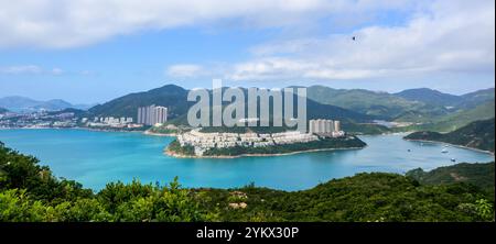 Une vue panoramique surplombant une baie avec une péninsule avec des bâtiments, des collines verdoyantes et quelques bateaux sur l'eau de Dragons Back Hike, Shek O. Banque D'Images