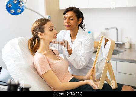 Jeune femme tenant le miroir pendant l'examen du cosmétologue Banque D'Images