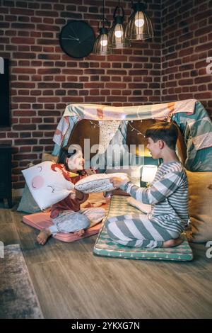 Enfants heureux avec pyjama s'amusant dans un combat d'oreiller sur tente d'abri faite à la main dans le salon Banque D'Images