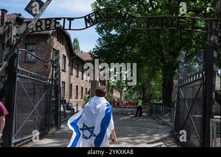 Jude avec le drapeau israélien dans le camp de concentration nazi allemand Auschwitz Birkenau. Écriture sur la porte d'entrée en allemand « Arbeit Mach frei » Banque D'Images