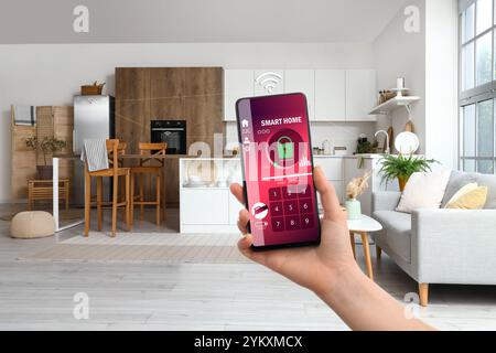 Main tenant téléphone mobile avec application ouverte de la domotique intelligente sur l'écran dans la cuisine Banque D'Images
