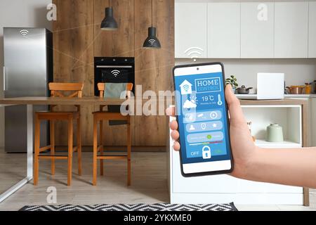 Main tenant téléphone mobile avec application ouverte de la domotique intelligente sur l'écran dans la cuisine Banque D'Images