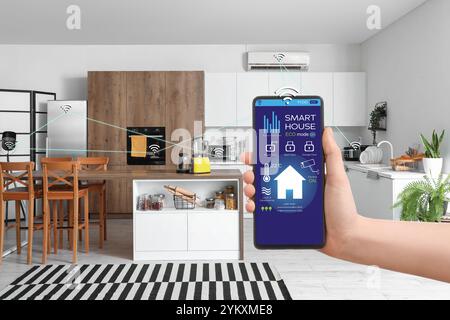 Main tenant téléphone mobile avec application ouverte de la domotique intelligente sur l'écran dans la cuisine Banque D'Images